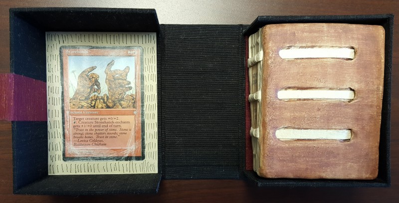 Clay-fired cover of the book on right, nestled into black cloth box with Magic: The Gathering Card on the left. 