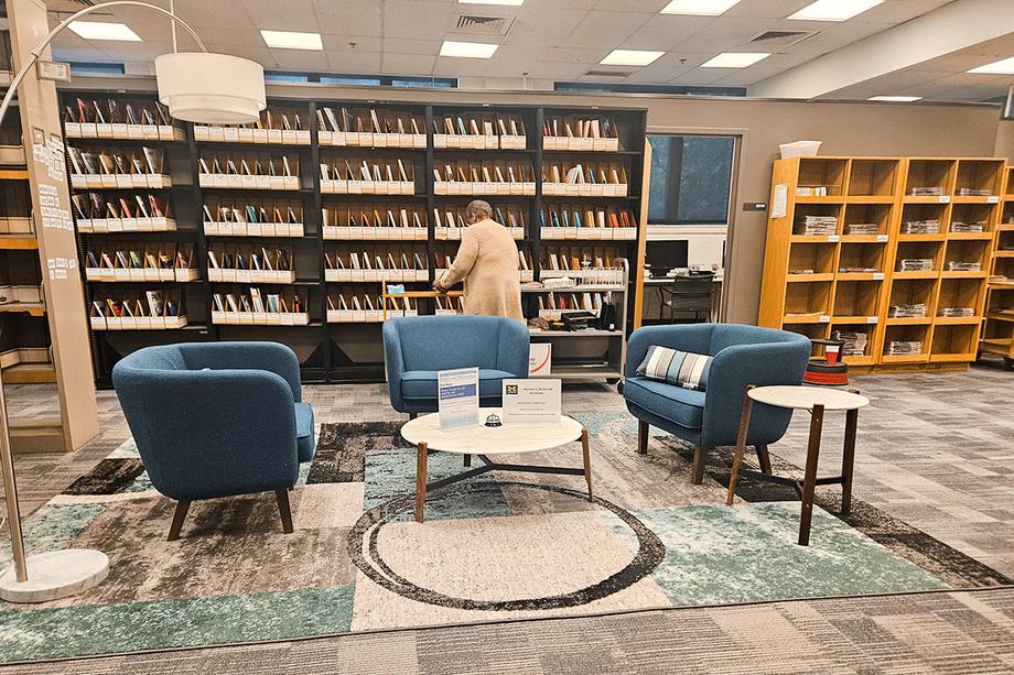 Comfy chairs around a small coffee surrounded by shelves of periodicals with a staff member in the background..