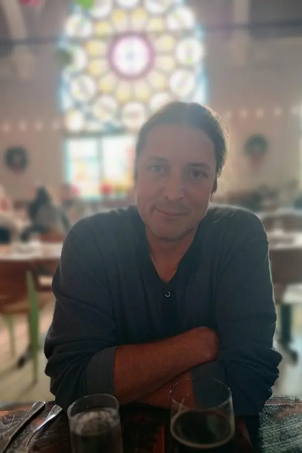 middle aged person seated at table with stained glass window in background