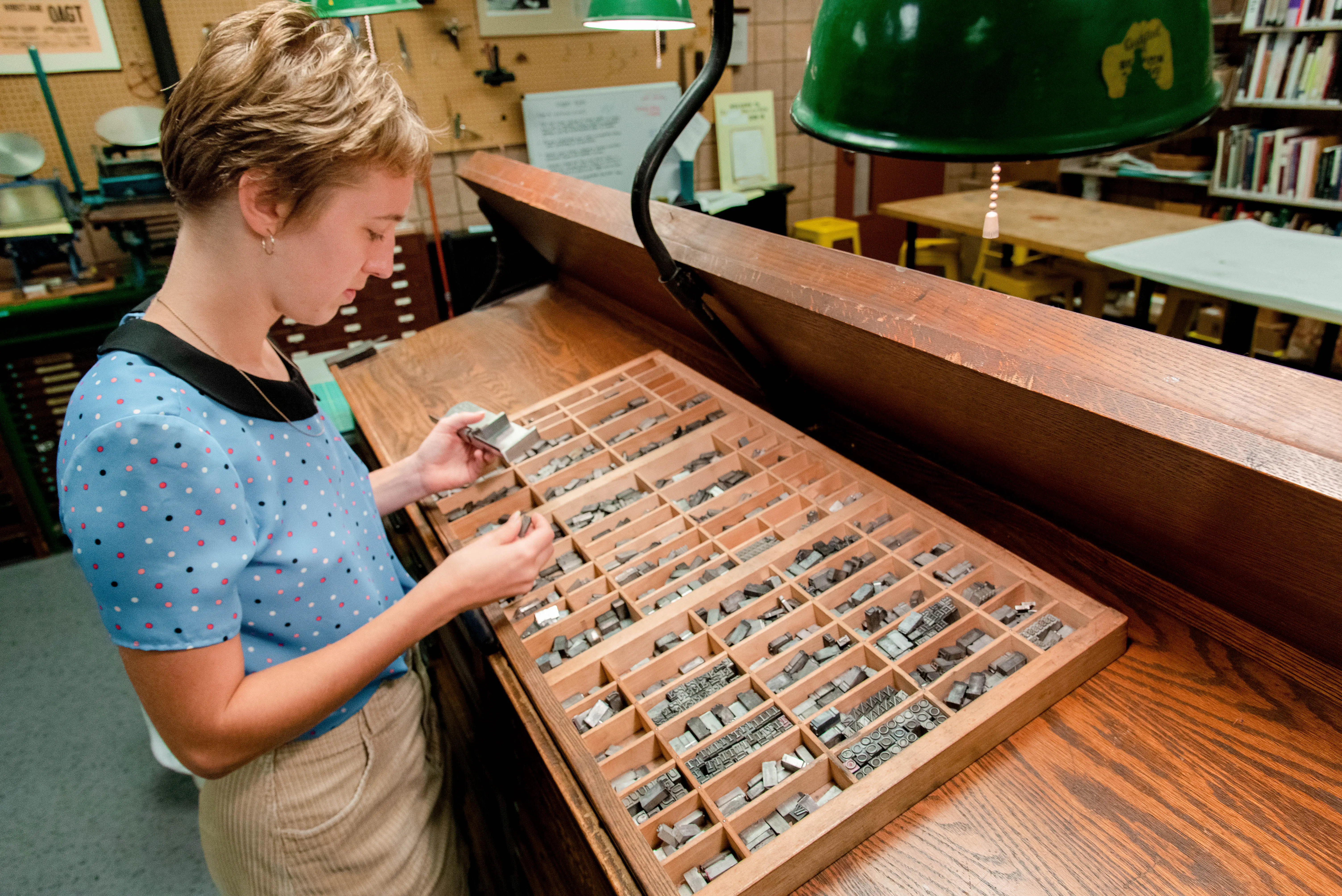 Student looking through a large set of metal type and putting them in a tray for printing.