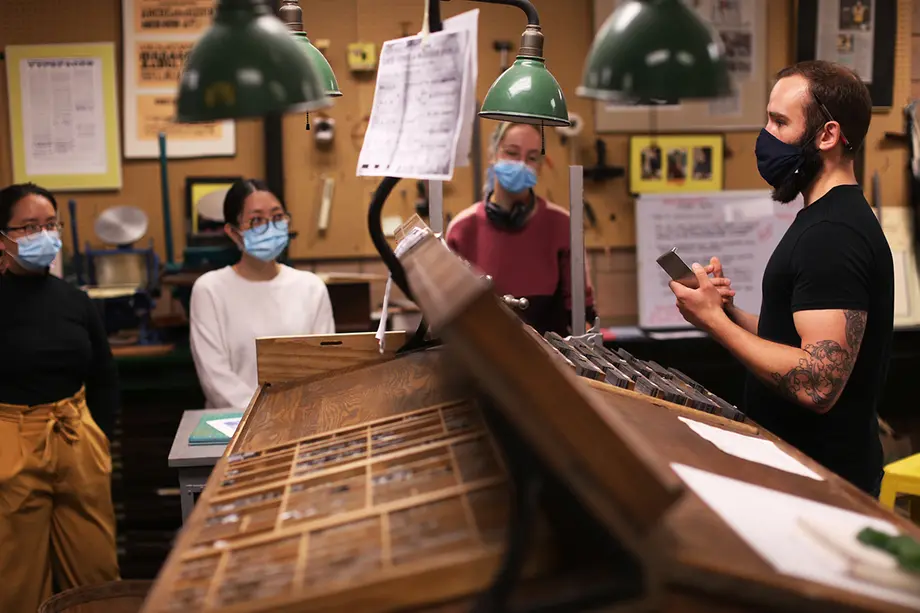 Masked instructor showing masked students moveable type in a wood case.