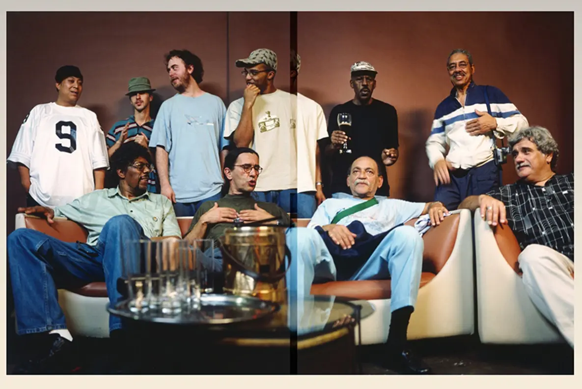An image of 10 men talking and laughing. Four are seated in the foreground and six are standing behind them.