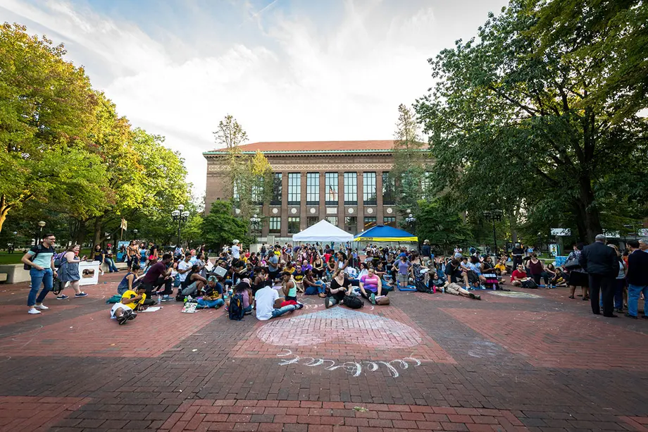 People gathered for a protest on the Diag with Hatcher Library in the background.