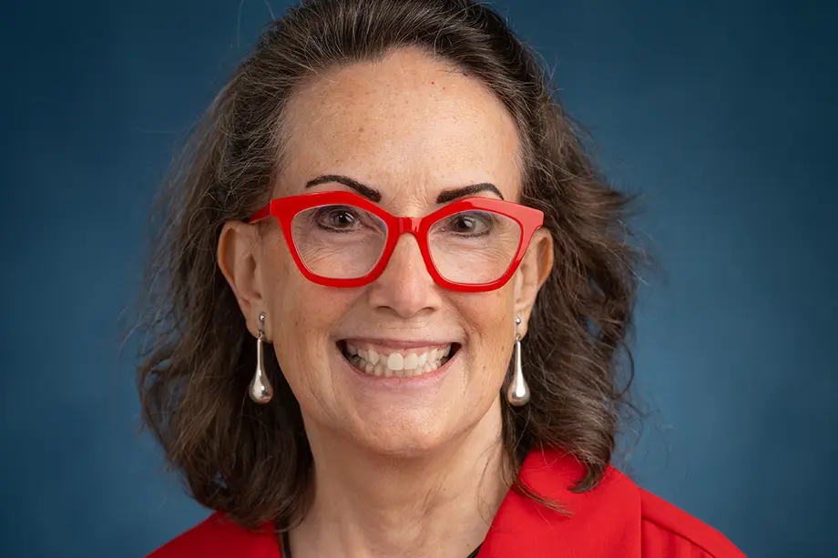 Headshot of Karen Downing wearing matching red-framed glasses and red top.