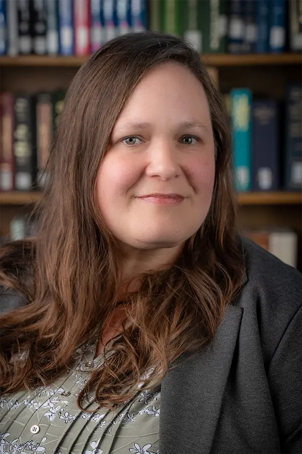 a picture of Merrie Fuller: a middle-aged white woman with long brown hair sitting in front of a filled bookcase