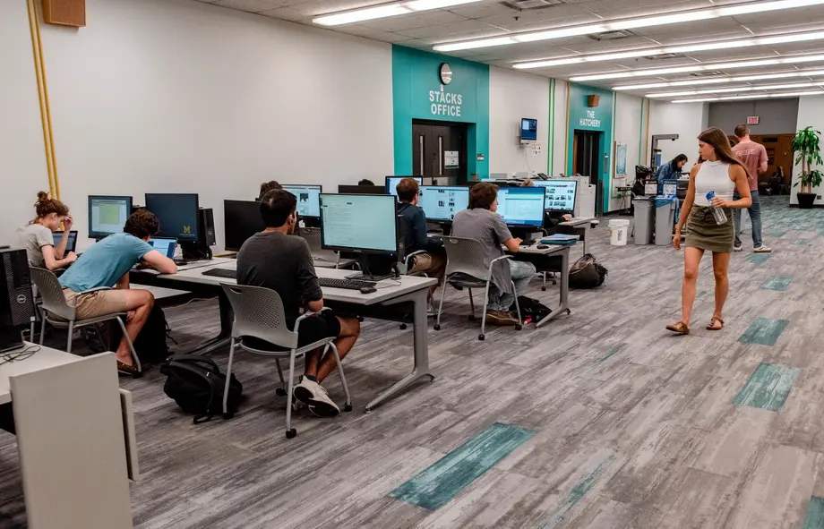 Students sitting at rows of computers while others walk by.