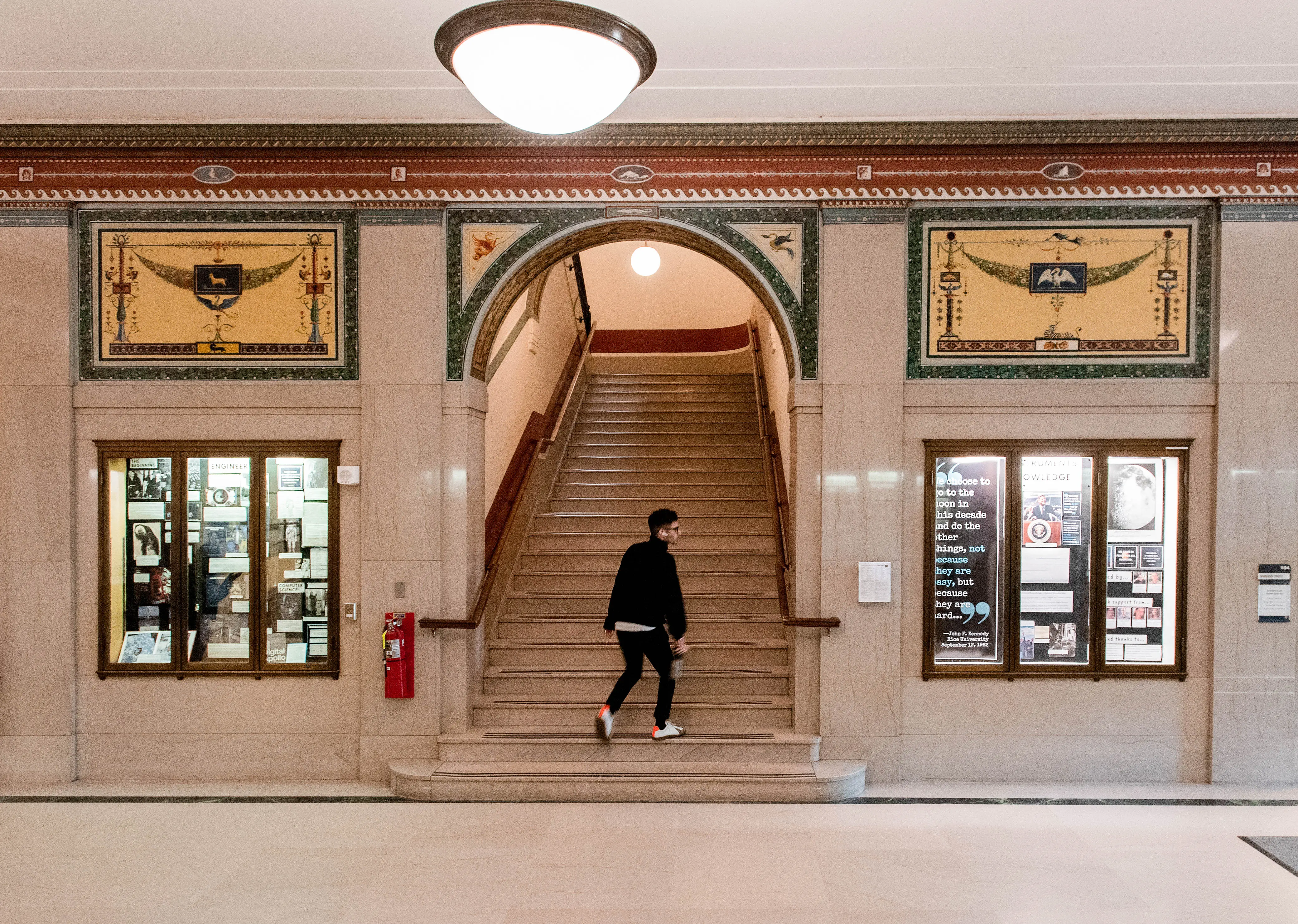 View of Hatcher North lobby exhibit cases with stairs in the center and a person walking up them.