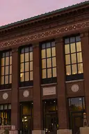 The front of Hatcher Library at sunrise with windows lit up.