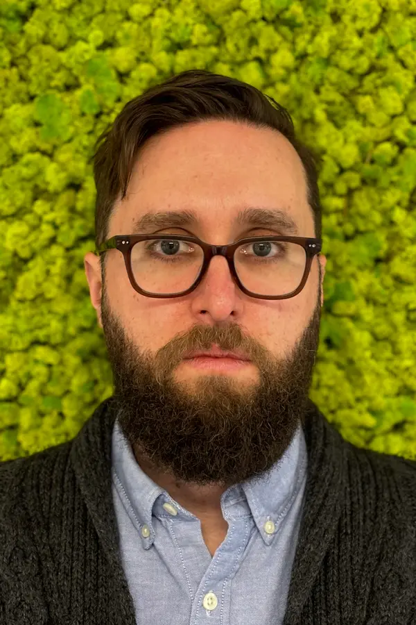 Photo of a bearded man standing in front of a mossy background