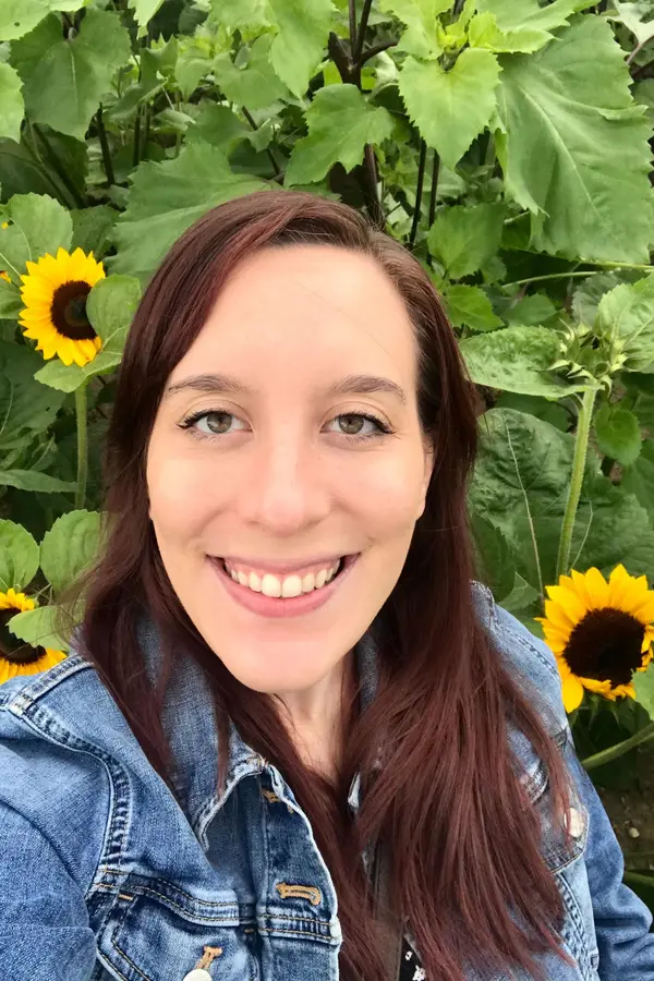 Photo of Katie Rokakis with sunflowers behind her
