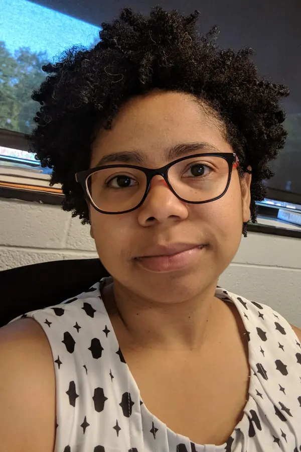 African-american woman facing camera wearing glasses and a white and black top.