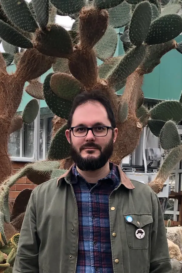 Photograph of Scott Witmer, a bearded white man idling before a large cactus