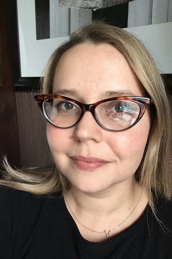 Photo of Kate Saylor, a white woman with medium length blonde hair, and glasses.