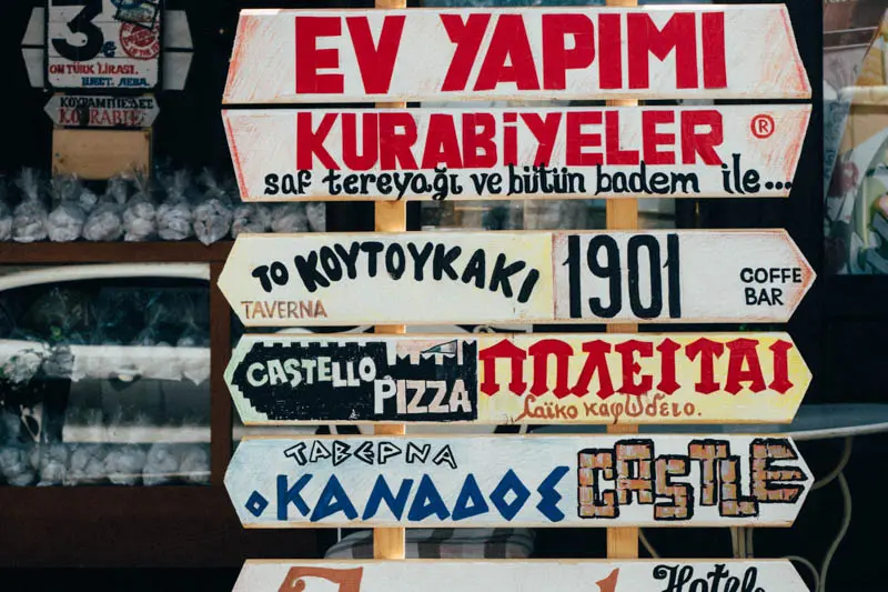 Stack of seven signs with a variety of messages written in Greek painted on them.