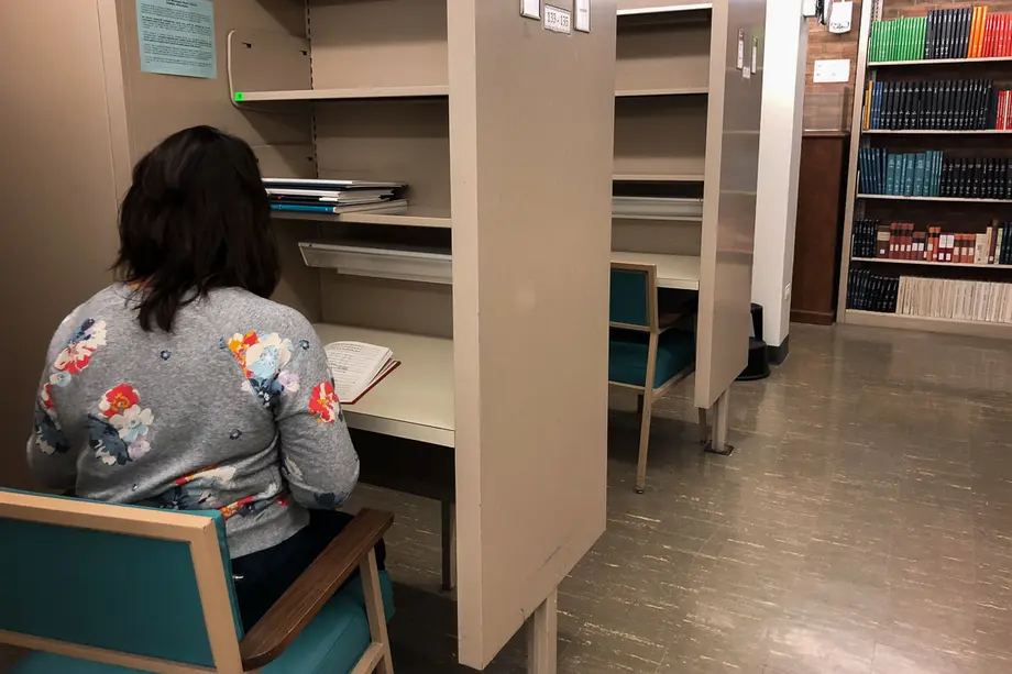 View from behind of sitting in a carrel in the Music Library with scores on the shelf in front of them.