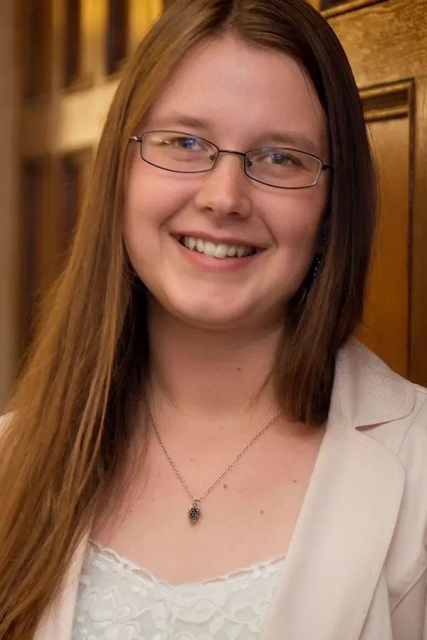 A young, white woman wearing glasses smiles warmly.