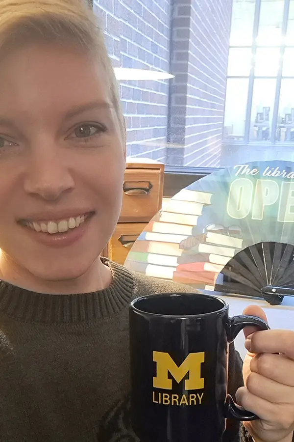 Photo of librarian Beth Havas, smiling and holding a University of Michigan Library mug.