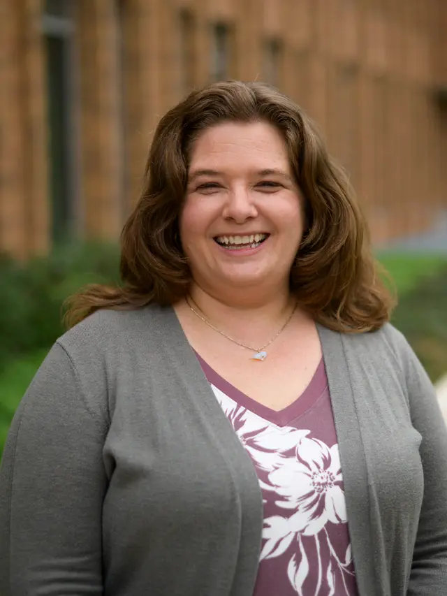 White woman in her 40s with dark blonde hair, wearing a librarian cardigan and laughing