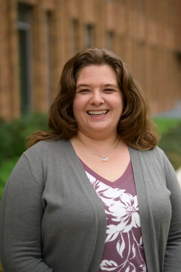 White woman in her 40s with dark blonde hair, wearing a librarian cardigan and laughing