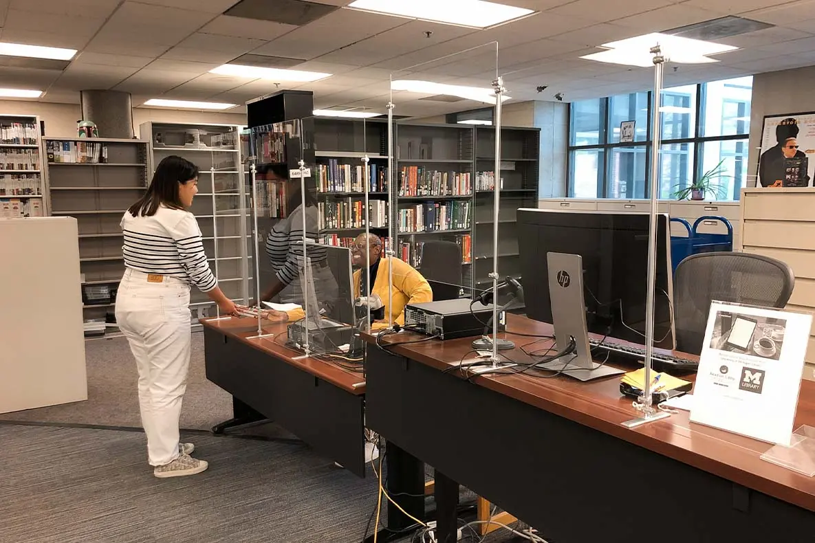 A student checking out materials from a staff member at the desk of the Askwith Media Library with shelves of materials in the background.