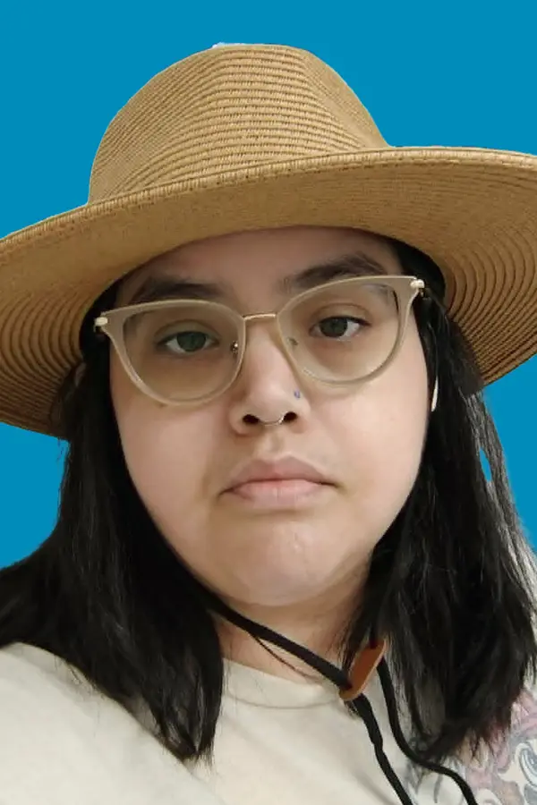 Woman with medium length black hair, glasses, and a beige hat with brim