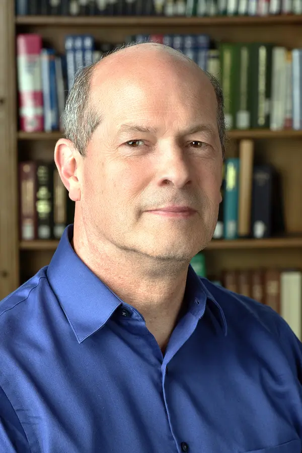 Photograph of Tim Utter, a white person with short gray-brown hair balding on top, wearing a blue shirt, in front of a bookcase.
