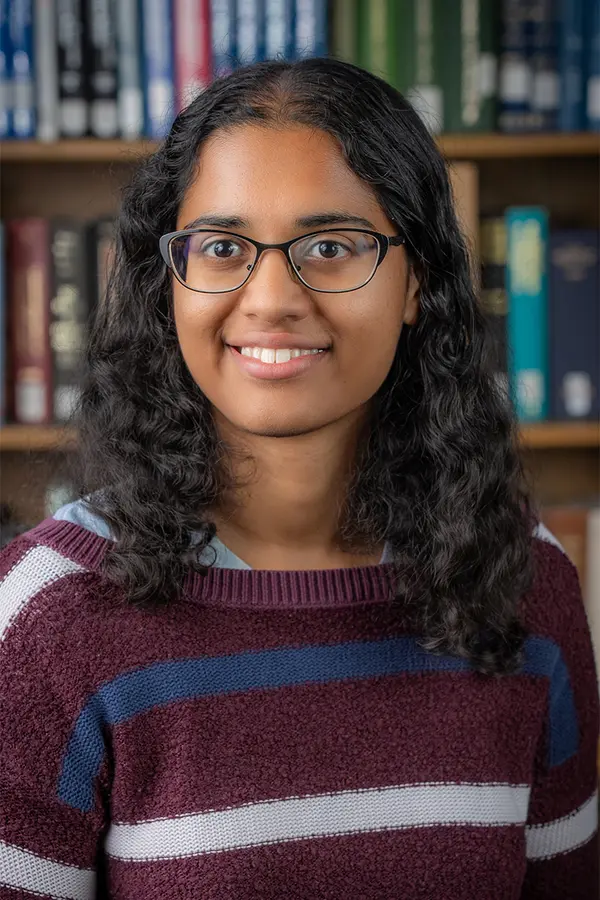 A headshot of a brown-skinned woman with curly, black hair and black glasses.. 