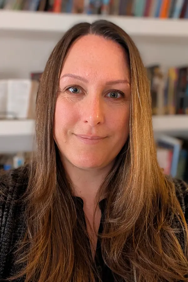 Photo of a white woman with long brown hair in front of a bookshelf