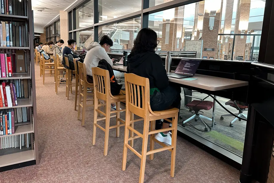 Students sitting high-backed wooden chairs at a bar height counter facing windows.