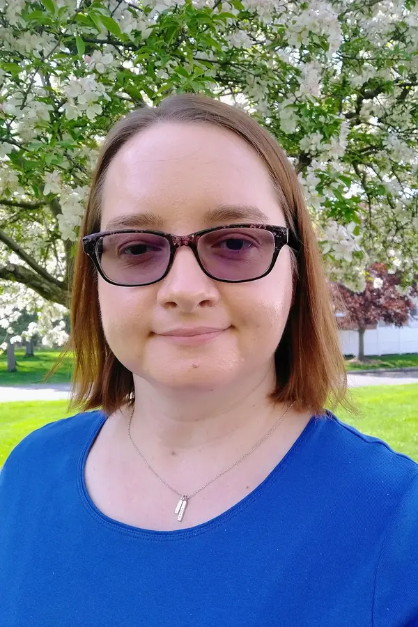 A white woman with glasses and shoulder-length brown hair, wearing a blue shirt.