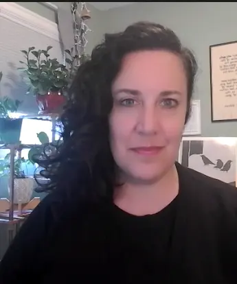 white woman with dark, curly hair wearing a black sweater pictured in her home office
