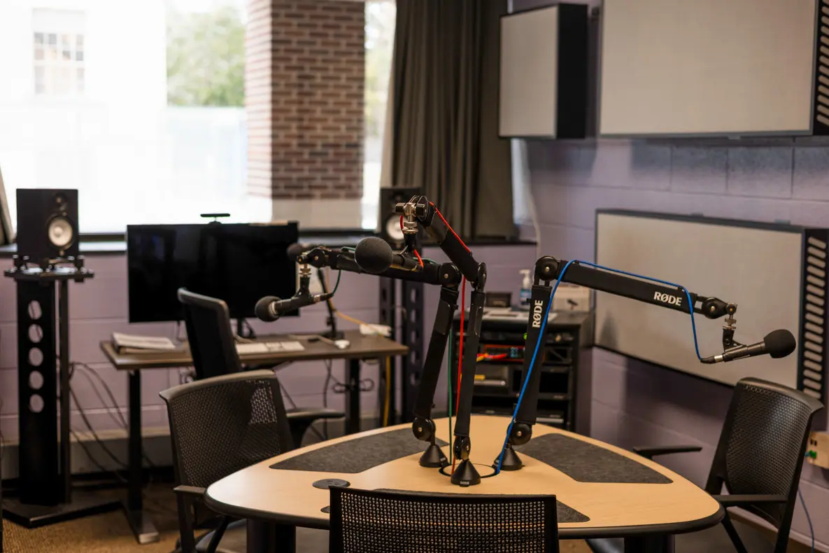 A table with attached microphones and a desktop computer in the background.