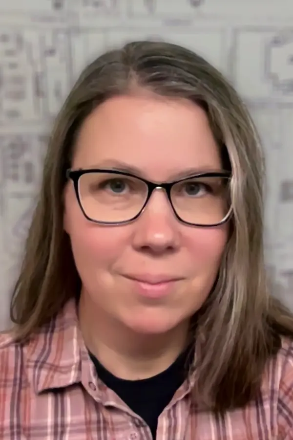 A photograph of Nicole Scholtz, a white woman with brown hair, wearing glasses, with a fuzzy black and white map as background