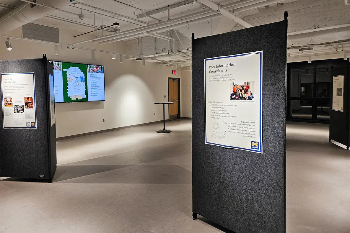 Three tall tripods with posters on them around the rooms and a screen on the wall displaying a slide.