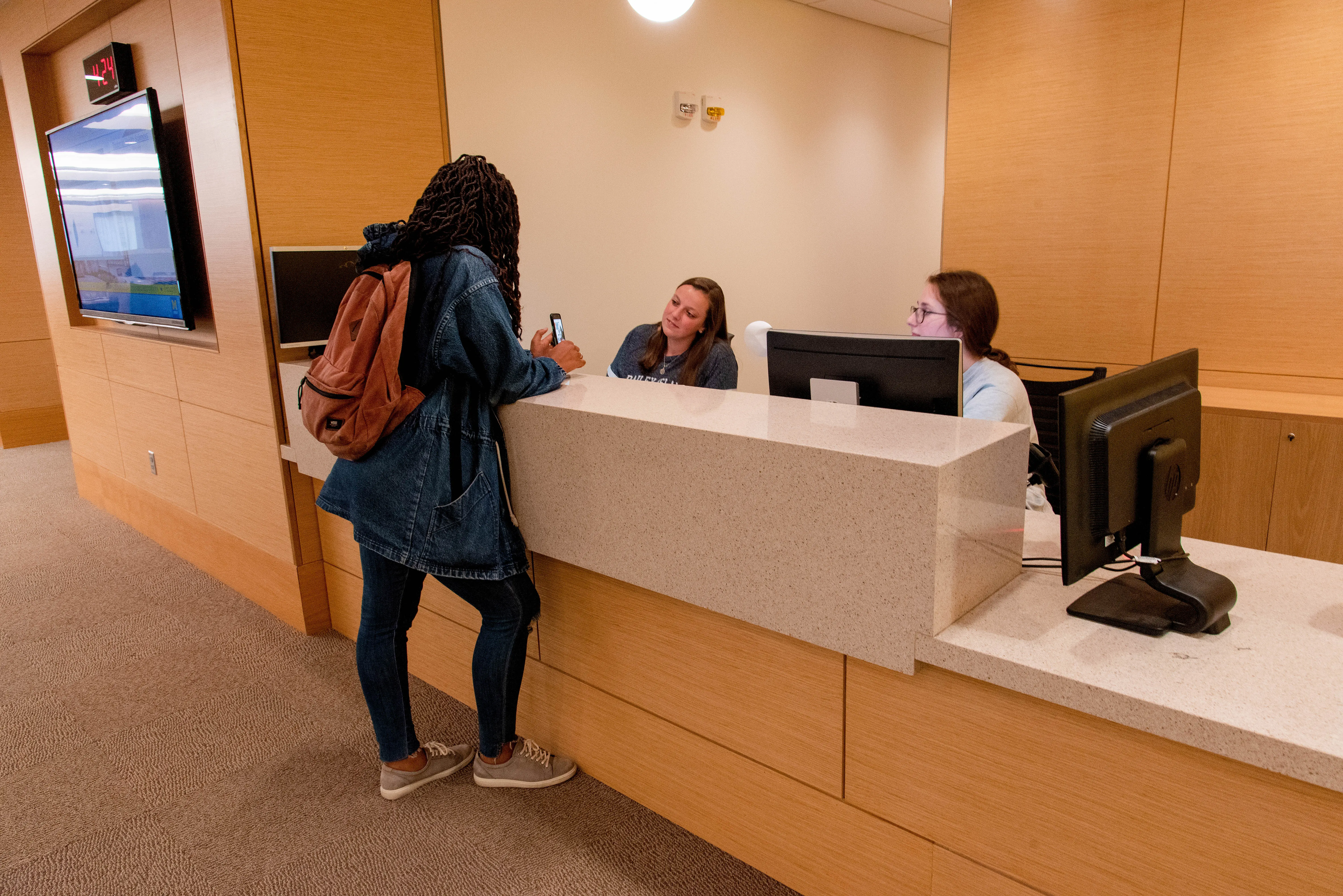 Two people sitting behind the Information Services desk at the Taubman Health Sciences Library talking to a student.