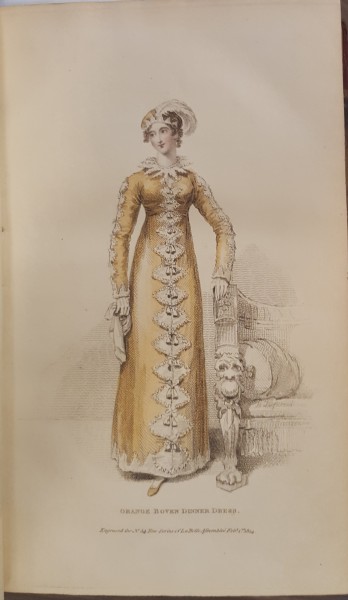 Woman standing, wearing an orange dress with white fan-shaped decorations down the front. 