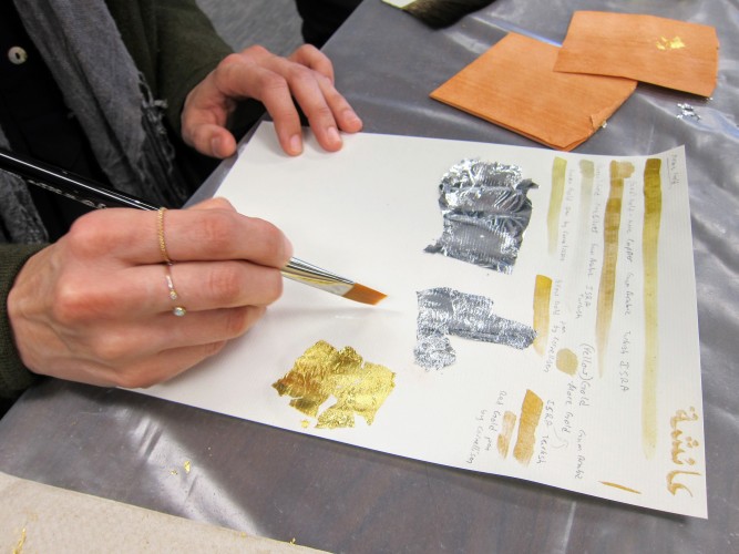 Participant holding brush over paper with bits of gold and silver leaf applied