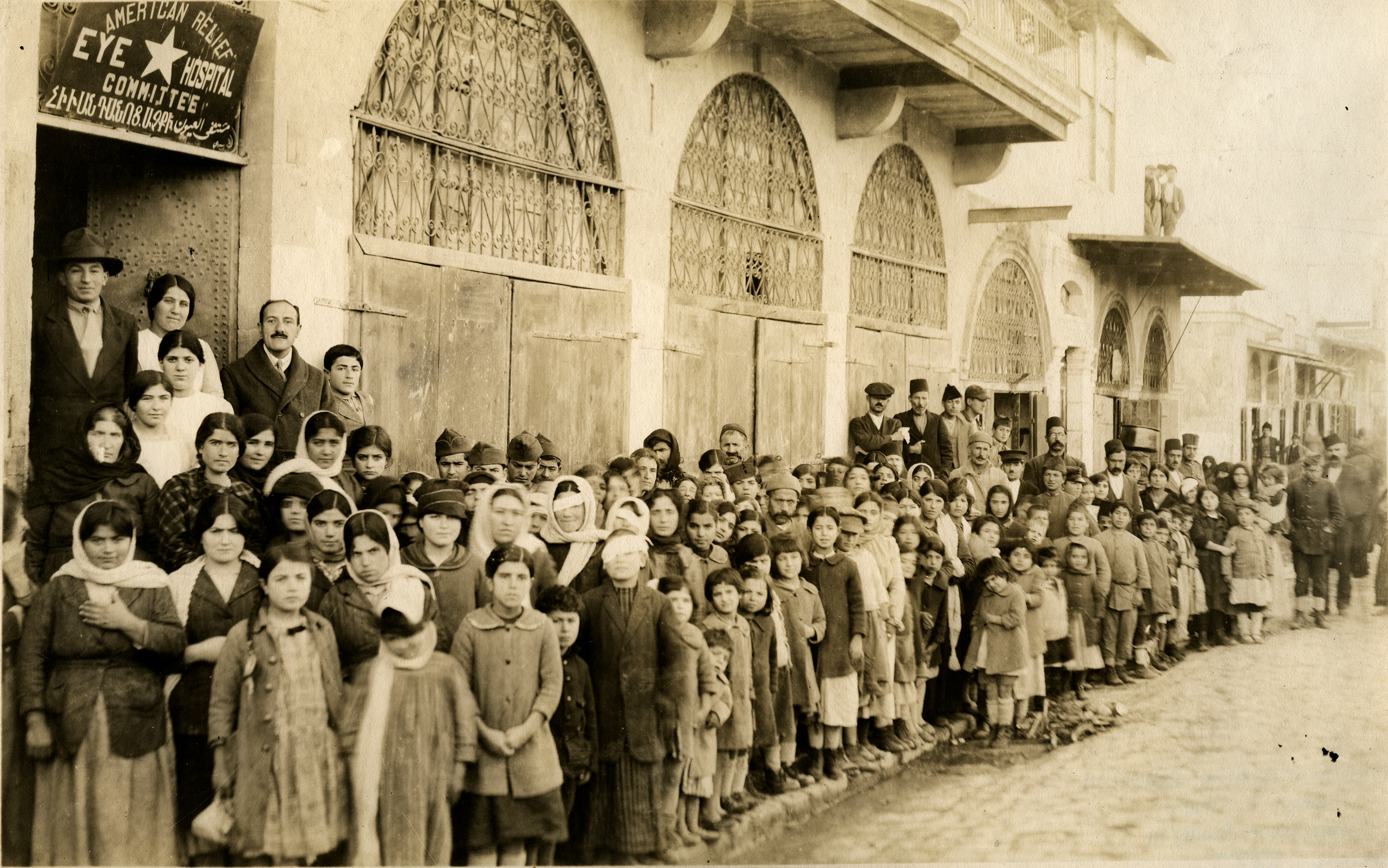 Line-up at the entrance to the A.C.R.N.E eye hospital, on the sidewalk. Dr. Tenner at right of door in back row at the left. January 7, 1920. Aleppo, Syria. Photograph by George R. Swain. Courtesy of the Kelsey Museum
