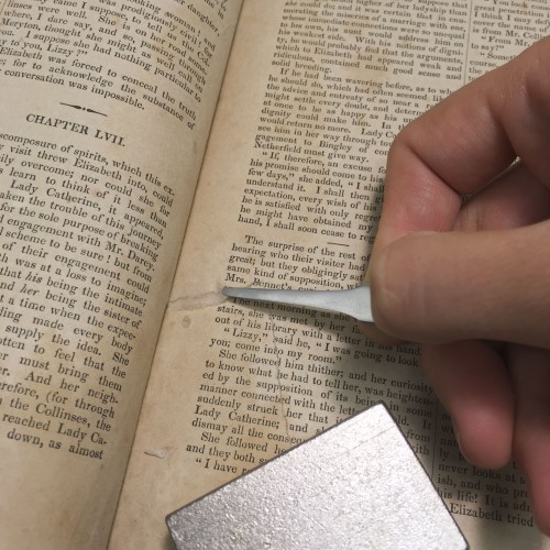 shows a thin metal tool (like large tweezers) being used to apply paper to mend a tear on an interior page