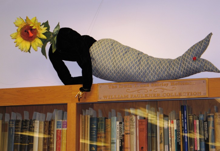 Figurine with a mermaid tale and a sunflower head, lounging on top of a bookcase