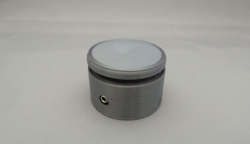 A cylindrical, grey button with a small hole for a auxiliary cable. The top of the button is light grey while the rest is a darker shade of grey. There is a small gap between the top portion and the bottom portion