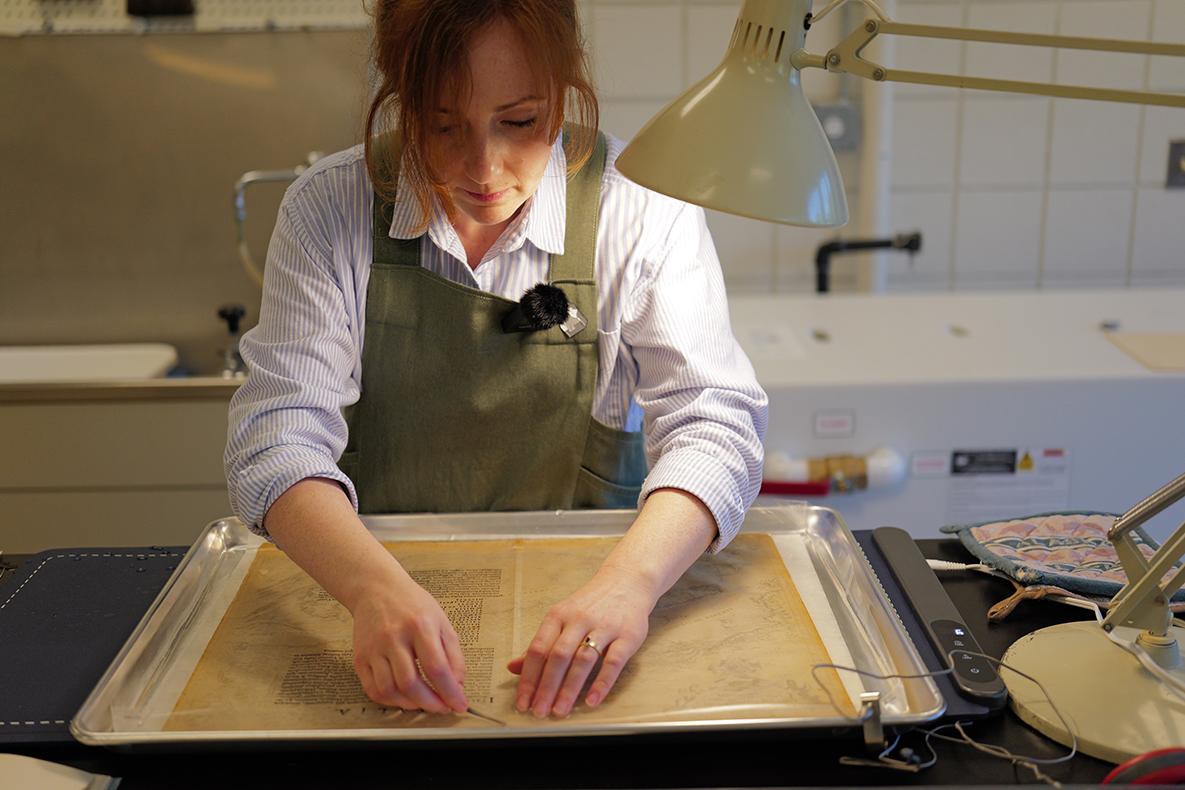 Woman leaning over a yellowed page in a water bath.