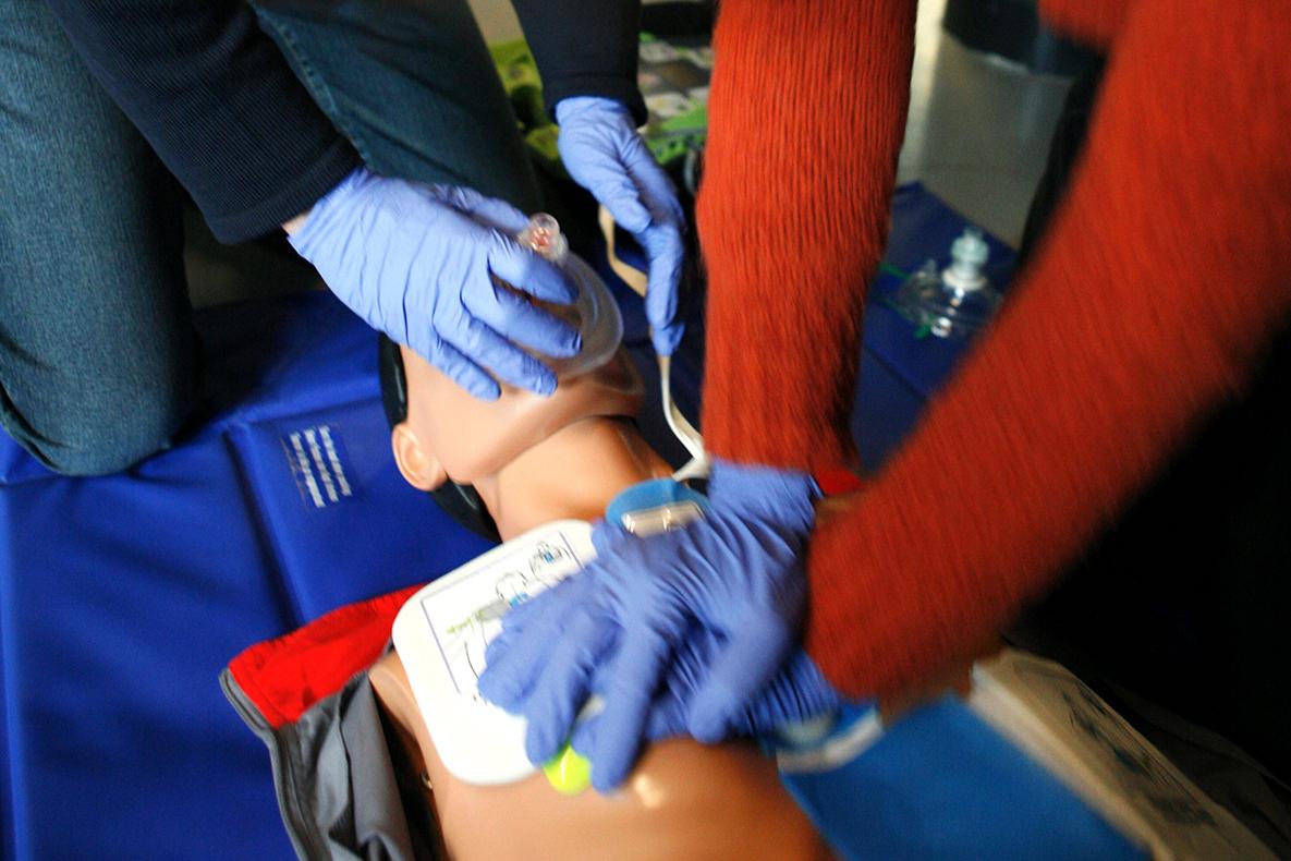Two hands wearing blue surgical gloves administer CPR on a dummy.