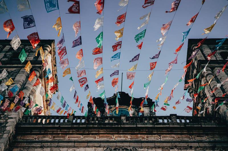 Low-angle photo of a church in Valladolid, Mexico with colorful flags hung.