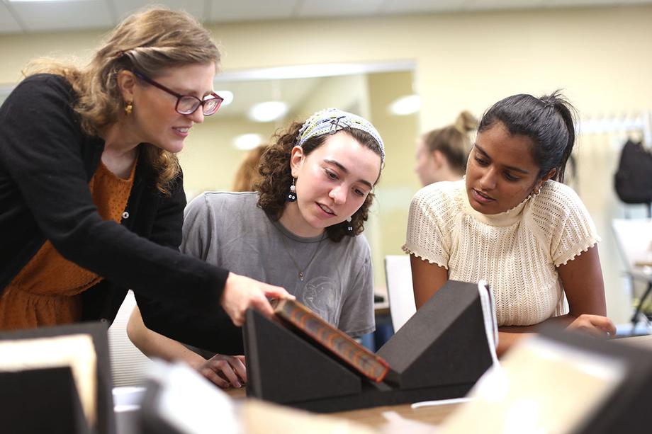 Three woman examine the cover of a book that's resting on a foam support.