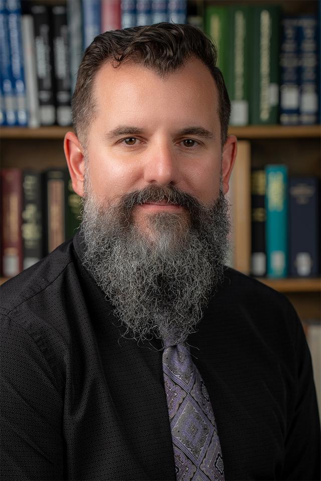 photograph of Stephen Griffes, a man with short brown hair and a long beard, wearing a black button down shirt, a light purple necktie, and a smile. 