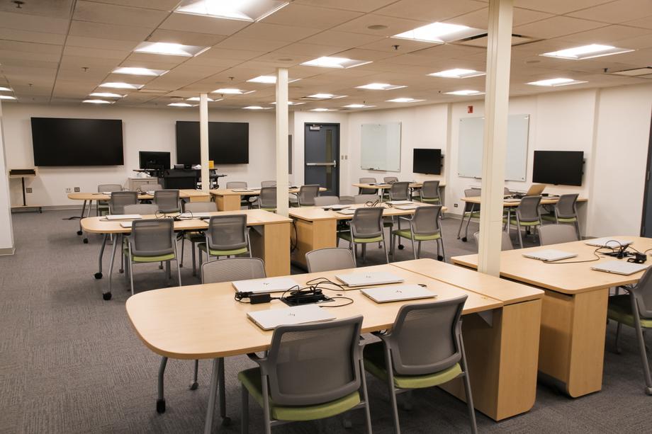 A large room with displays on the far wall and tables with laptops on them.