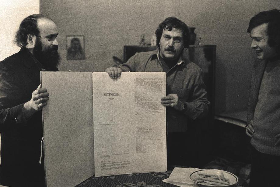 Black and white photograph of two men holding a large, open book and a third man standing to the side.