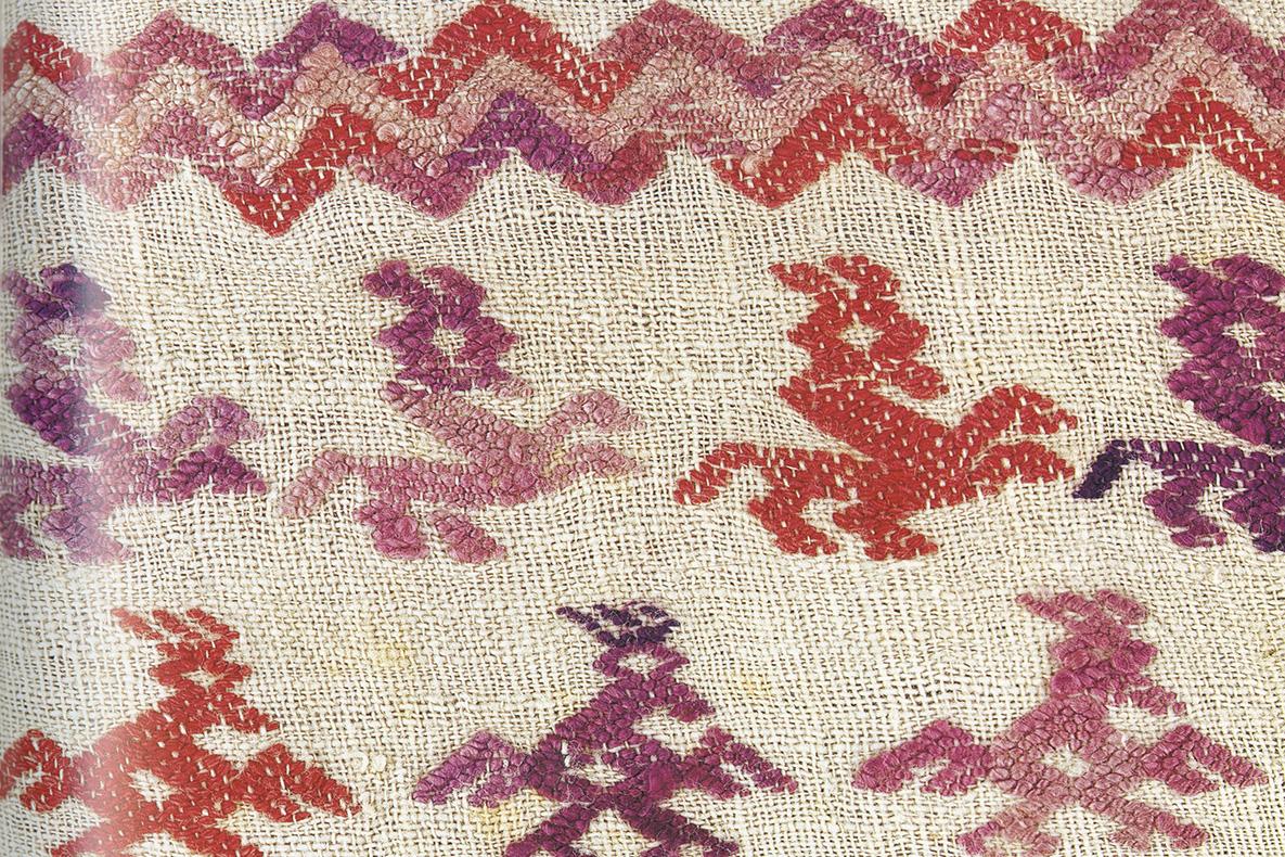 Weaving of a zigzag and creatures in reds and purples on a beige background.