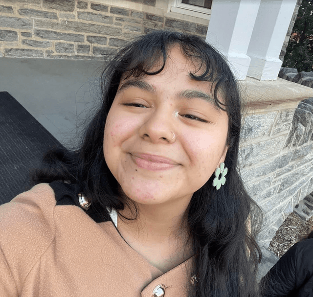 Selfie of Jaimie with long-hair, bangs, and wearing a beige coat. 